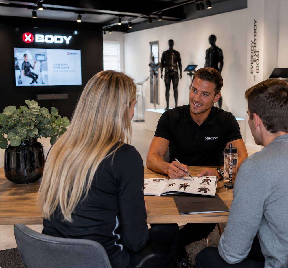 Professionele EMS-trainer toont een draadloos droog EMS-pak in een moderne studio, met premium apparatuur en heldere, uitnodigende belichting.